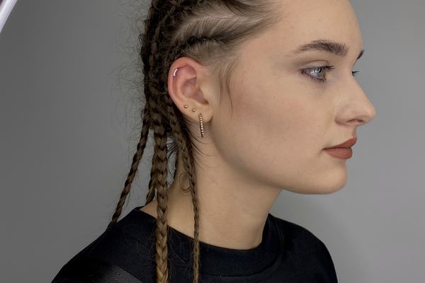 Profil klientky v salóne VeAn v Košiciach; ľavé ucho s helix a dvoma lalôčikovými piercingmi – malé zlaté štifty a huggie krúžok; ukážka bezpečného, profesionálneho piercingu a vhodného výberu šperkov.