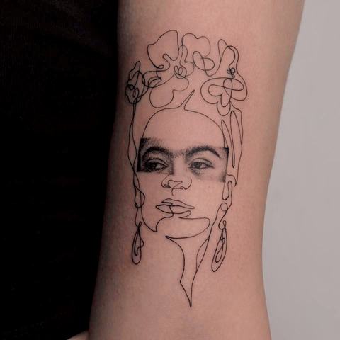 A fine line portrait tattoo framed by loose floral shapes and delicate facial details. The minimal black outline gives the design an artistic, sketch-like feel.