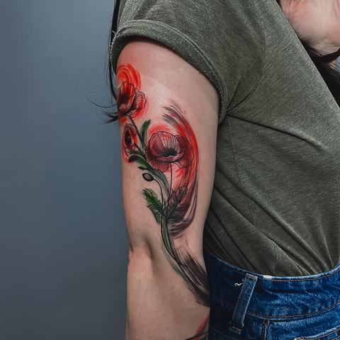 A floral upper-arm tattoo with vivid red flowers, green leaves and free black strokes. The loose composition gives the piece movement and expressive character.
