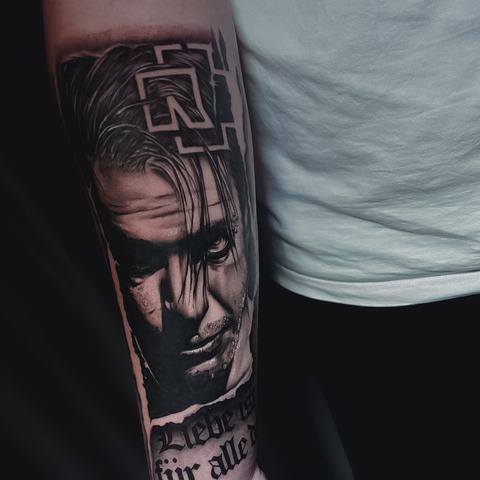 A dramatic black-and-grey portrait on the forearm with deep shadows, strong facial features and a geometric symbol above the head for added intensity.