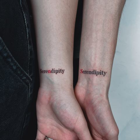 Matching “Serendipity” tattoos placed near the wrists, using elegant lettering in black and red for a simple, personal and coordinated design.