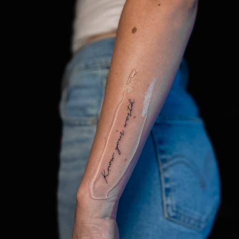1. A minimalist script tattoo placed along the forearm, combining a handwritten phrase with subtle light details for a clean, personal and understated design.