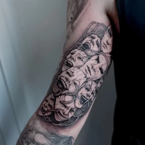 A complex black-and-grey forearm piece made of multiple expressive faces. Layered emotions, fine contours and shading create a dynamic visual rhythm.
