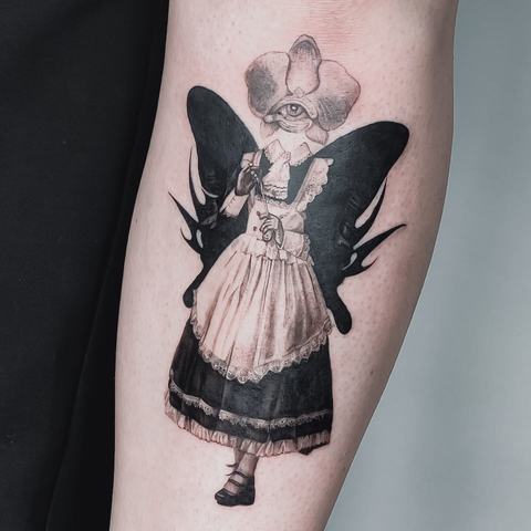 An unusual fairy-inspired tattoo featuring a delicate figure in a dress with dark wings. Fine details and bold black shapes create a distinctive illustration.
